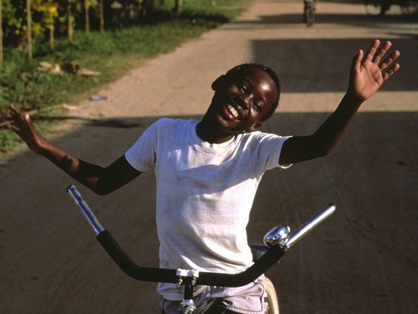 A happy boy with outstretched arms on a bicycle.